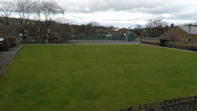 Lush green bowling green surrounded by trees and buildings under a cloudy sky in Oxenhope, Yorkshire.