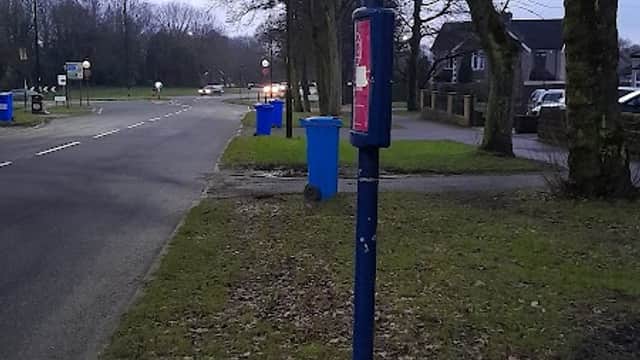 Bus stop sign near Norton Lane, with a blue phone box and recycling bins along a tree-lined road in Greenhill.