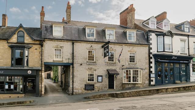 Historic stone building with a black sign, surrounded by other shops and a blue sky in Pickering, Yorkshire.