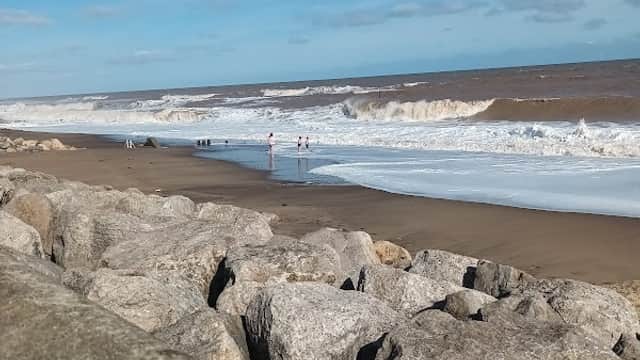 View of a sandy beach with waves crashing, rocky foreground, and a clear blue sky in Withernsea, Yorkshire.