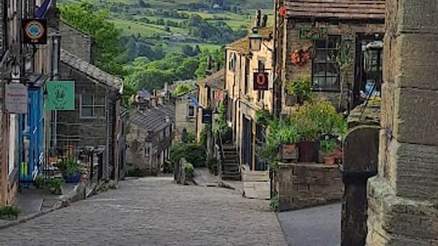 Cobblestone street lined with stone buildings, greenery, and hills in the background, capturing a serene Yorkshire village scene.