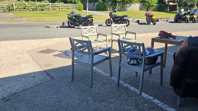 View from a grocer's patio with empty chairs, parked motorcycles, and greenery in the background under a clear blue sky.