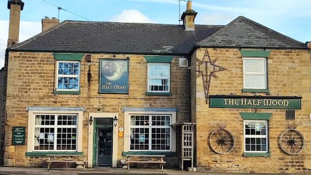 Traditional stone pub with green window frames, wooden benches, and a sign reading "The Half Moon" in Barton, Yorkshire.