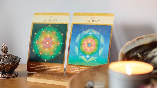 Two cards titled "Healing" and "Fertility" displayed on a wooden surface beside a lit candle and decorative items.