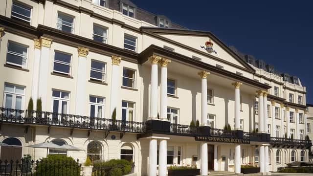 Elegant white facade of Crown Spa Hotel, featuring grand columns and ornate detailing under a clear blue sky.