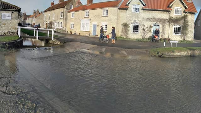 Charming stone cottages in Hovingham with a shallow stream, pedestrians, and strollers near a quaint village setting.