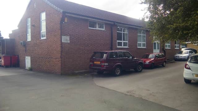 West Bretton Village Hall, a brick building with windows, surrounded by parked cars and greenery.
