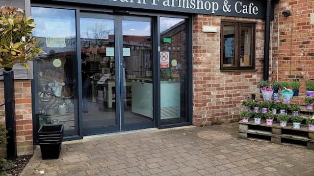 Cedar Barn Farm Shop & Cafe entrance with glass doors, brick walls, and potted plants in front.