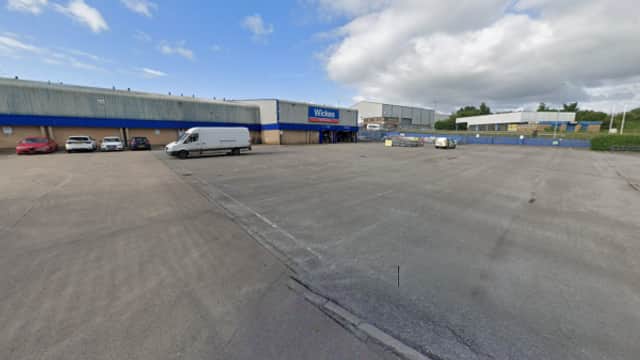 Empty car park with a van and a few cars, surrounded by industrial buildings under a partly cloudy sky.