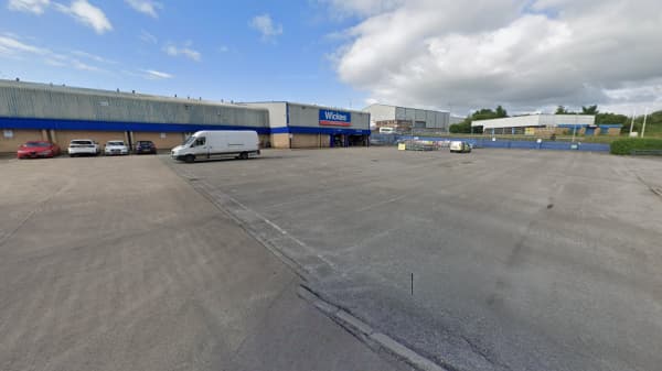 Empty car park with a van and a few cars, surrounded by industrial buildings under a partly cloudy sky.