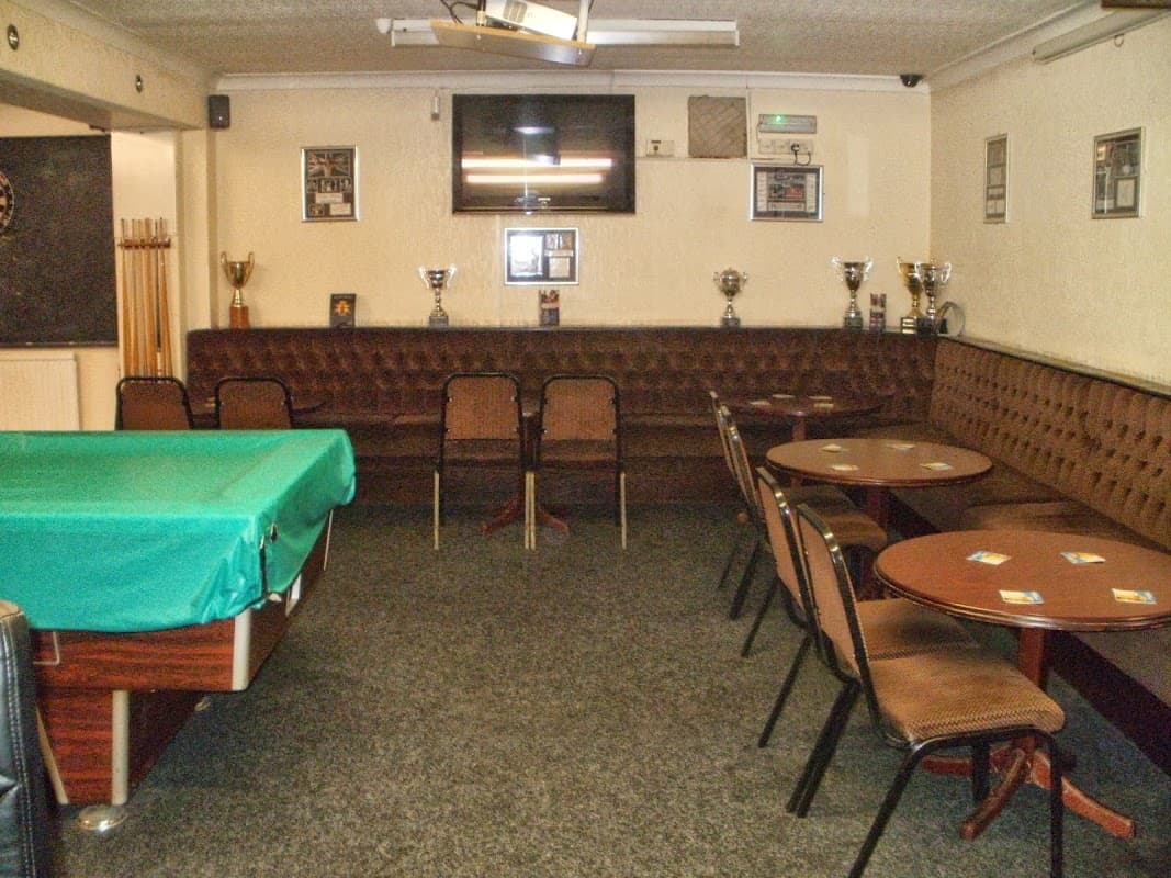 Interior of Park Social Club with a green pool table, brown seating, tables, trophies, and a wall-mounted TV.