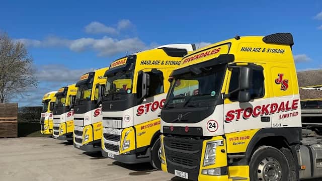 Five yellow trucks lined up, featuring "Stockdale Ltd" branding, parked on a concrete surface under a blue sky.