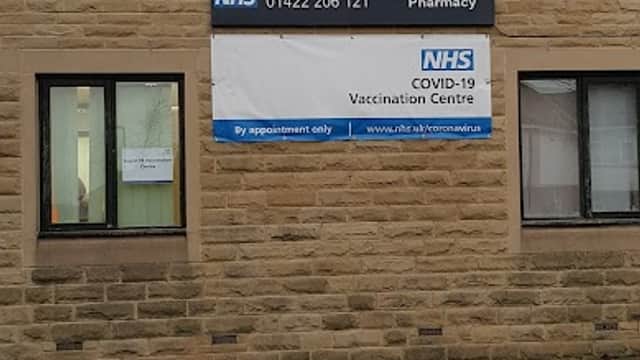 Signage for Northowram Surgery featuring NHS contact details and COVID-19 vaccination information on a stone building.