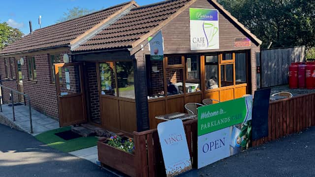 Cozy cafe with wooden exterior, green signage, and outdoor seating in Yafforth, Yorkshire, surrounded by trees.