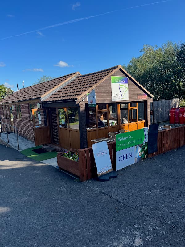 Cozy cafe with wooden exterior, green signage, and outdoor seating in Yafforth, Yorkshire, surrounded by trees.