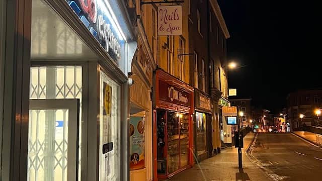 Tesco Express storefront illuminated at night, with nearby shops and streetlights in Knaresborough, Yorkshire.