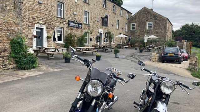 Two motorcycles parked in front of The Punch Bowl Inn, a stone building with outdoor seating and trees in Crackpot, Yorkshire.