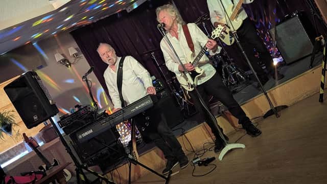 Live band performing at Meltham Liberal Club, with colorful lights and musical instruments on stage.