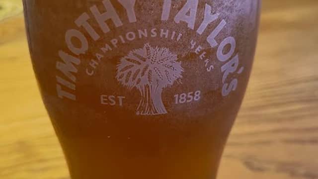 A pint of Timothy Taylor's beer on a wooden table with a coaster beneath it.