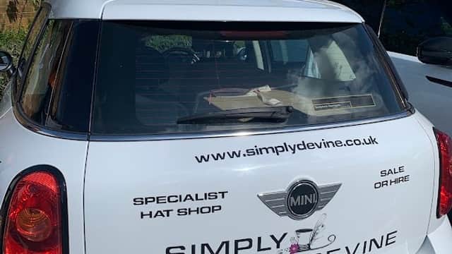 A white Mini car parked in a nursery car park with a sign for a hat shop on the rear window.