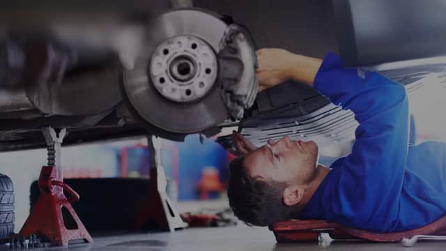 A mechanic in blue coveralls working under a car, focusing on the brake assembly in a garage setting.