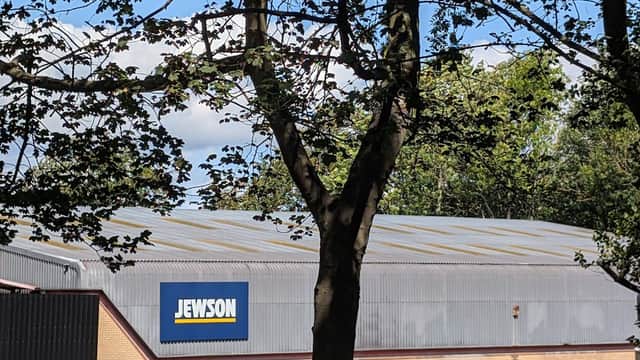 Jewson building with large blue sign, surrounded by trees and a parking area with cars in Harrogate, Yorkshire.