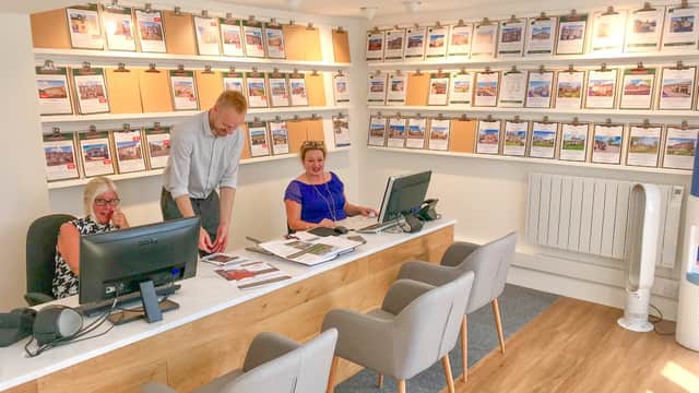Bright office space with three staff members at desks, showcasing property listings on clipboards on the wall.