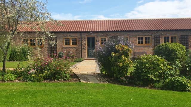 Charming brick cottage with a red tiled roof, surrounded by colorful gardens and lush greenery in Bessingby, Yorkshire.