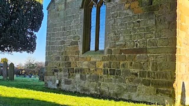 Stone building with a bell tower, arched windows, and a grassy area, surrounded by trees in Welbury, Yorkshire.