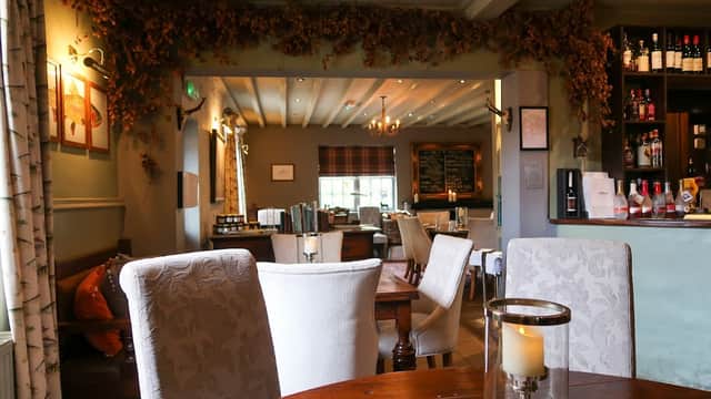 Cozy bar interior with wooden tables, chairs, and a well-stocked counter, adorned with warm lighting and decorative foliage.