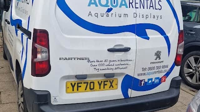 White van with "Aqua Rentals" logo, featuring blue waves and text about aquarium displays, parked near a pharmacy.