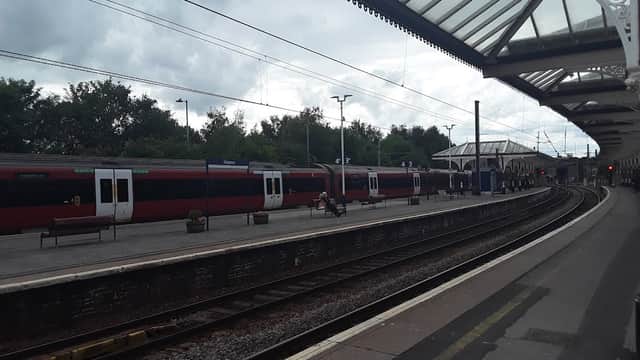 Skipton Railway Station features two red trains, a covered platform, and a cloudy sky in Yorkshire.