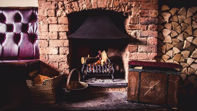 Cozy fireplace with a black hood, wooden logs stacked beside it, and a vintage chest in a warm, inviting interior.