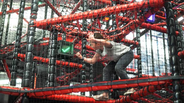 Person navigating a red and black indoor climbing structure with nets and ropes, focused and balancing carefully.