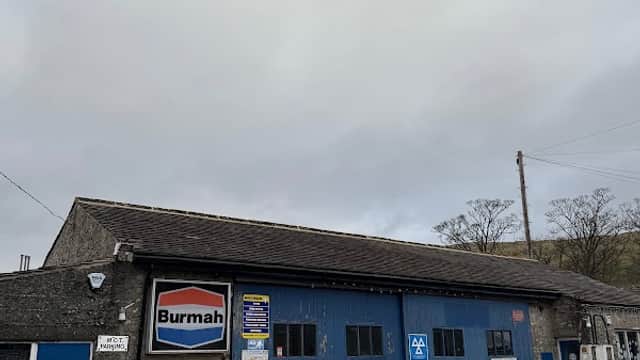 Kettlewell Garage with blue doors, a Burmah sign, and a white Mini car parked outside under a cloudy sky.