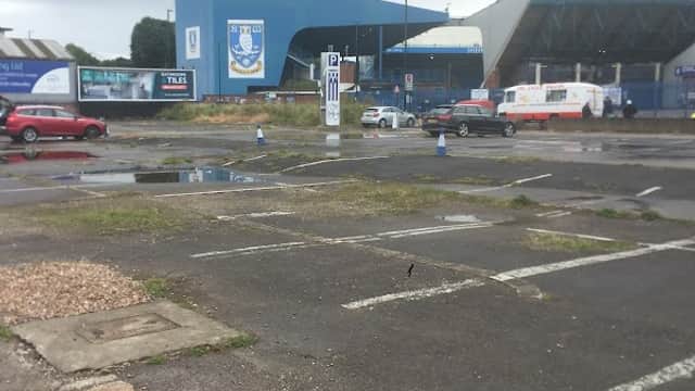 Empty car park with puddles, featuring a blue building and Sheffield Wednesday signage in the background.