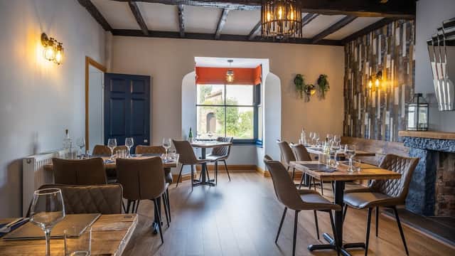 Cozy bar interior with wooden beams, tables set for dining, and a large window overlooking greenery.