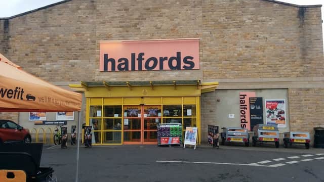 Halfords store exterior in Kirkstall, Leeds, featuring large signage, parking area, and promotional banners.