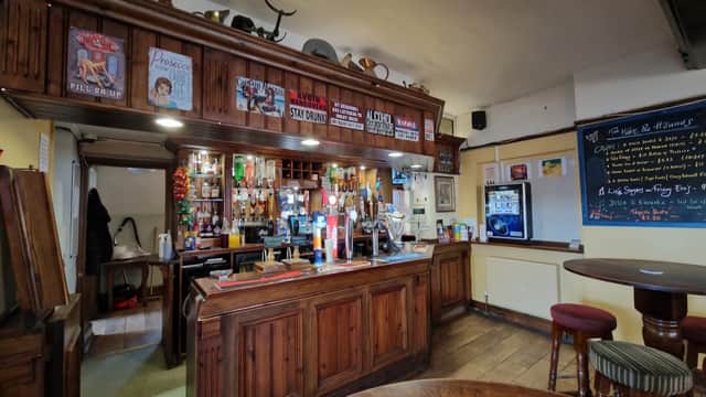 Rustic wooden bar with various drinks, vintage posters, and a chalkboard menu in a cozy restaurant setting.