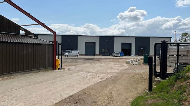 Business park with industrial buildings, parked vehicles, gravel driveway, and partly cloudy sky in Asenby, Yorkshire.