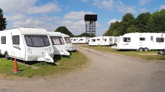 Caravans parked in a spacious lot surrounded by trees, with a cloudy blue sky overhead.