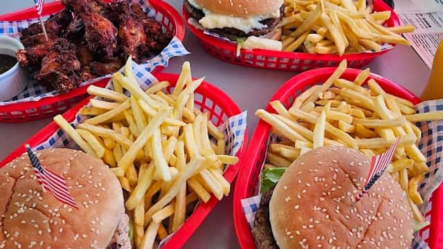 Burgers with American flags, crispy fries, and chicken wings served in red baskets on a diner table.