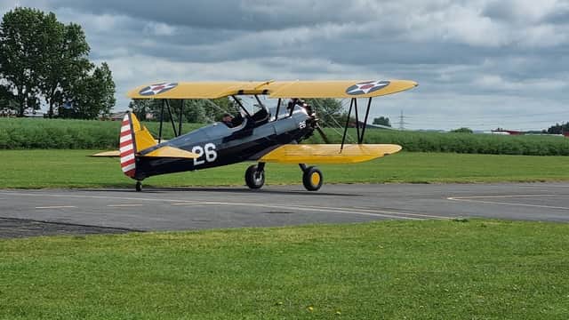 A vintage biplane with a yellow wing and black body taxis on a grassy airstrip at Breighton Aerodrome.