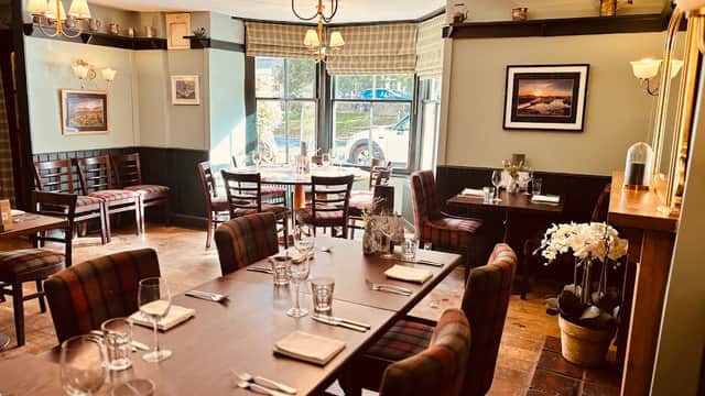 Cozy restaurant interior with wooden tables, plaid chairs, and soft lighting, featuring floral decor and scenic wall art.
