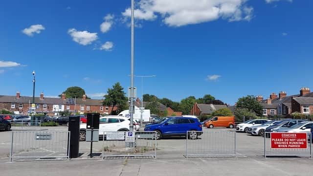 Car park with various vehicles, blue sky, and a sign instructing coaches not to park. Residential buildings in background.