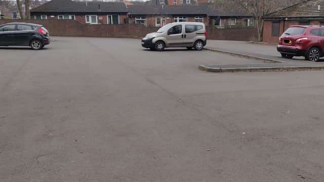 Empty car park with a few parked cars and surrounding buildings in a residential area.