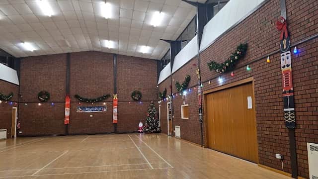 Spacious event venue with wooden flooring, decorated walls, and festive lights, featuring a Christmas tree in the corner.