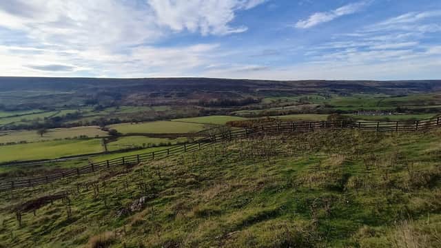 Rolling green hills under a blue sky with wispy clouds, bordered by a wooden fence in Rosedale Abbey, Yorkshire.