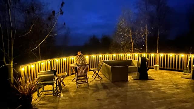 Cozy outdoor deck with warm lighting, seating, and trees under a night sky at Yurtshire Fountains in North Yorkshire.