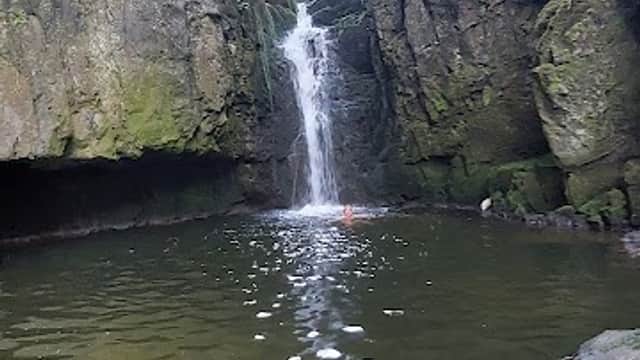 Waterfall cascading into a clear pool, surrounded by rugged stone cliffs and lush greenery in Langcliffe, Yorkshire.